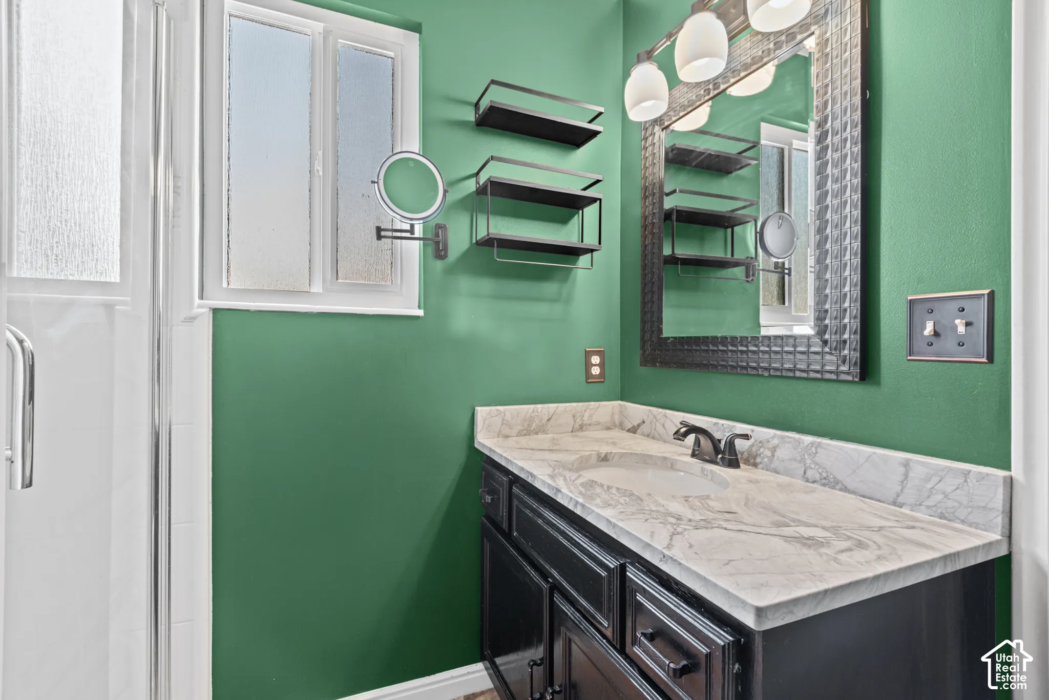 Vanity with a light-toned stone countertop and integrated sink, framed mirror with overhead lighting, and built-in shelving