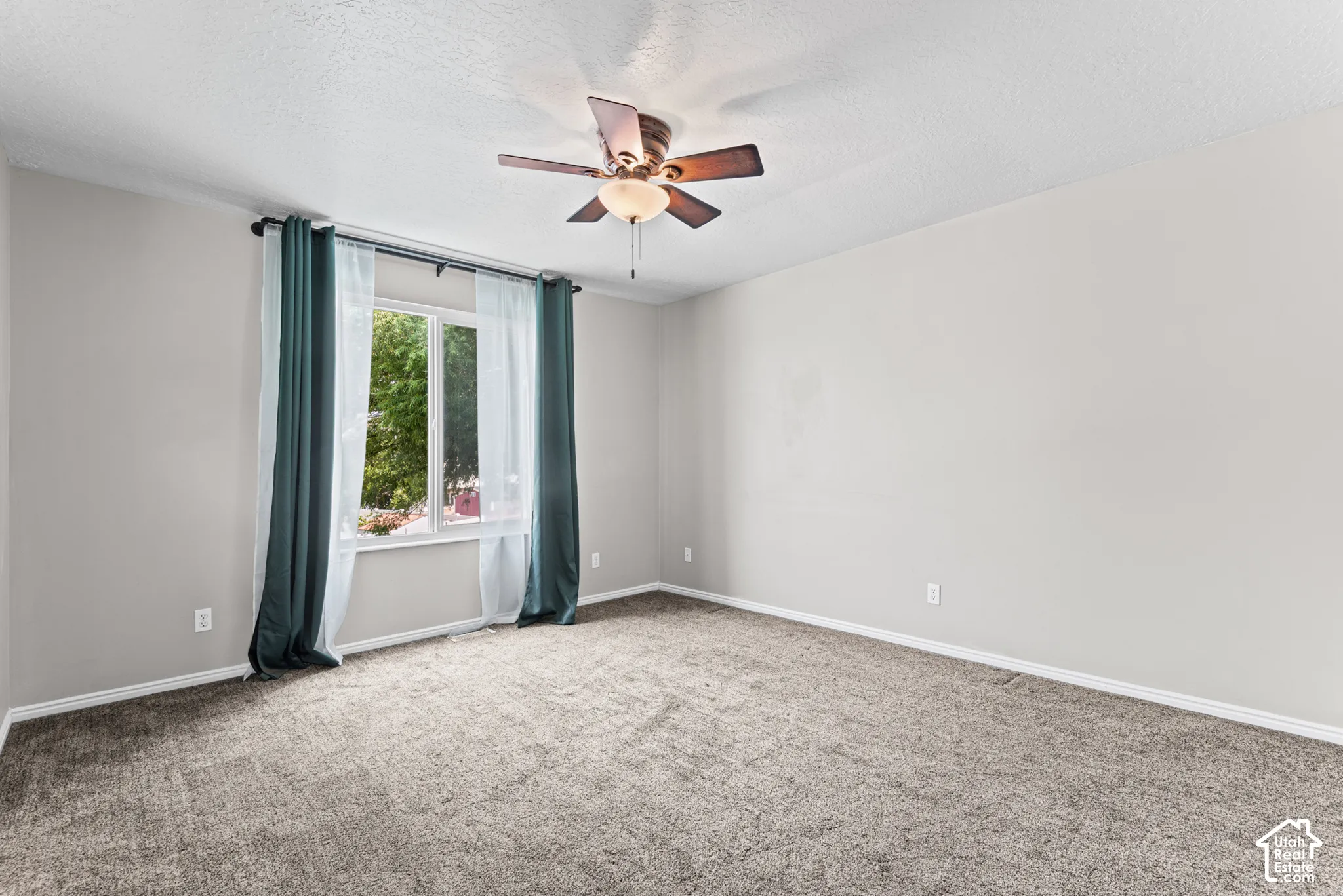 Expansive room with neutral carpeting, a large window, and a ceiling fan with integrated lighting