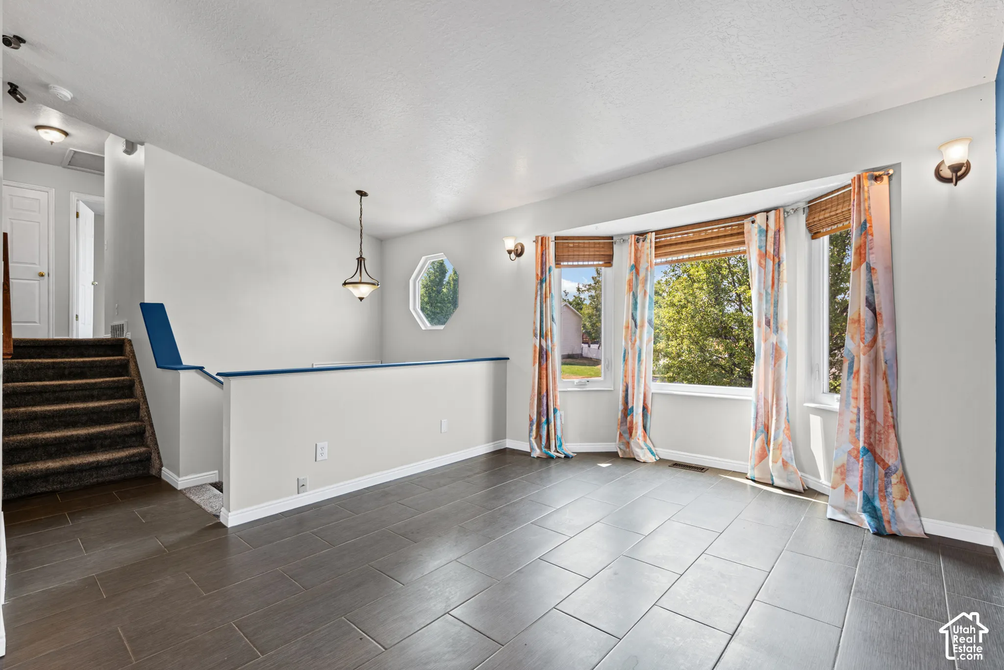 Expansive bay window, octagonal accent window, dark tile flooring, staircase with carpeted treads, and a polished nickel pendant light fixture