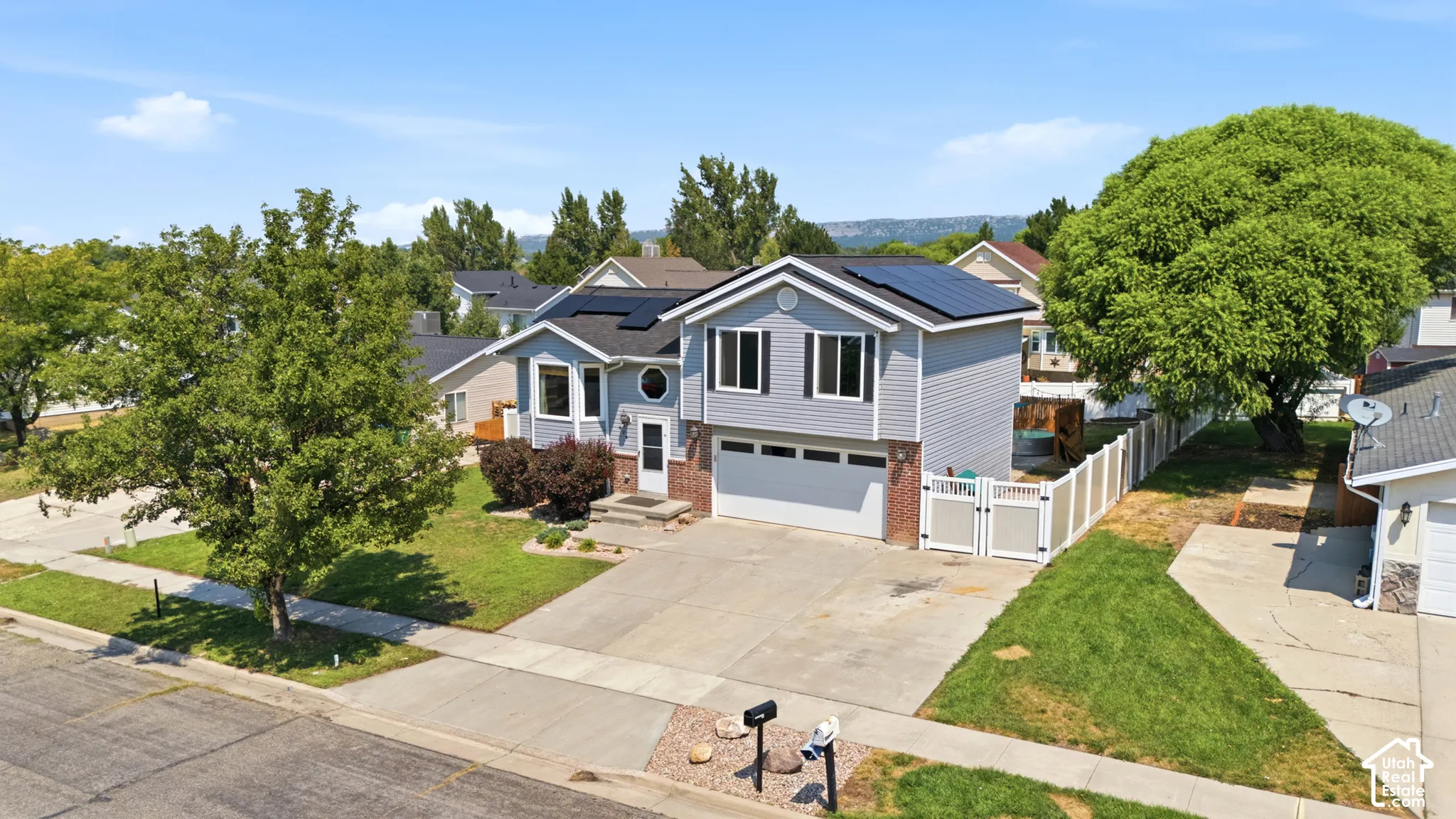 Two-story residence featuring light gray siding, a dark shingle roof with solar panels, an attached garage, and a white privacy fence