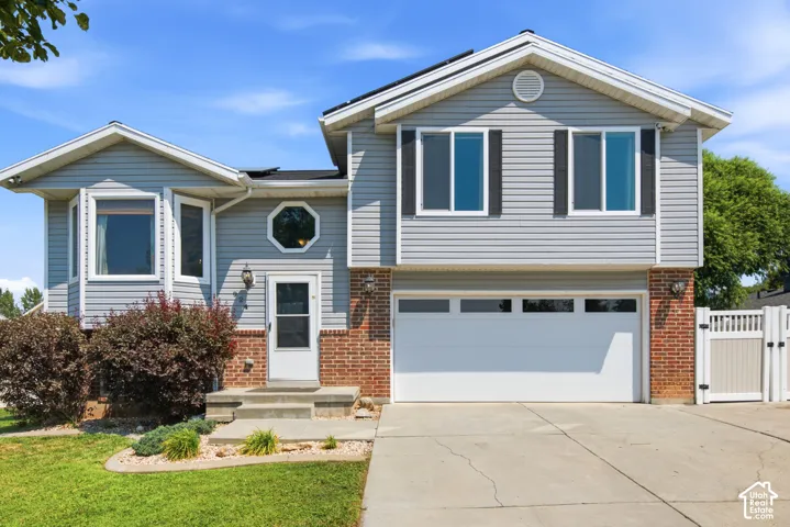Exterior featuring light gray siding, red brick accents, an attached garage, a bay window, and a white picket fence