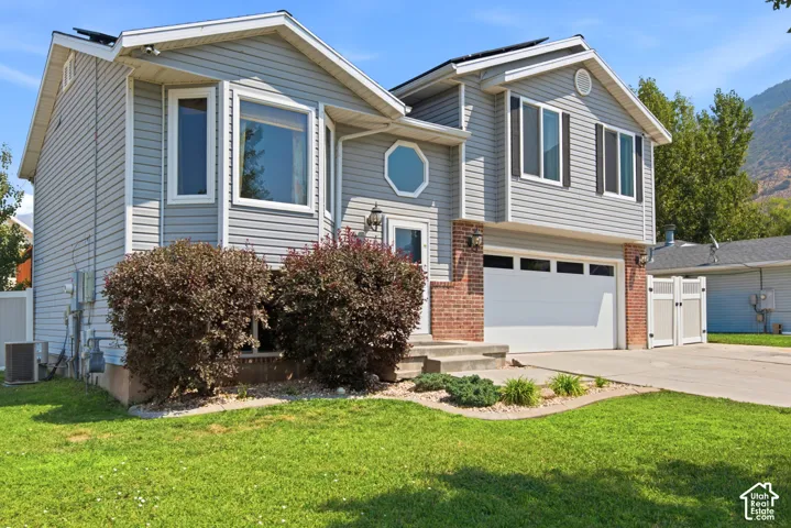 Gray siding exterior with a red brick accent, a two-car garage, a concrete driveway, and mature landscaping
