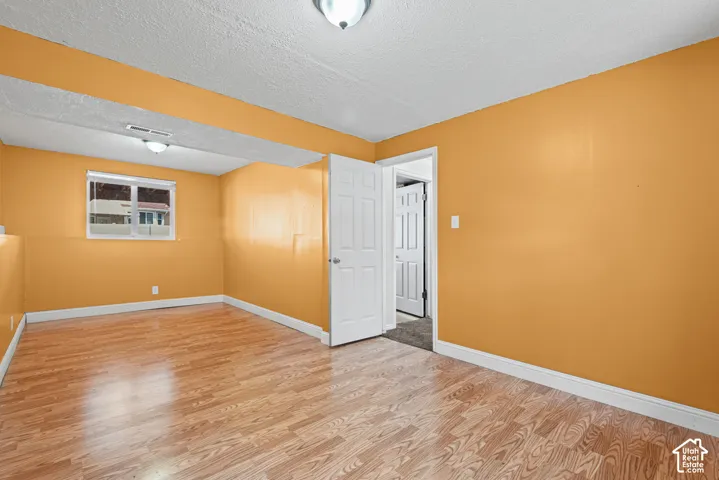 Spacious interior room with wood-finish flooring, a single window, and a white paneled door