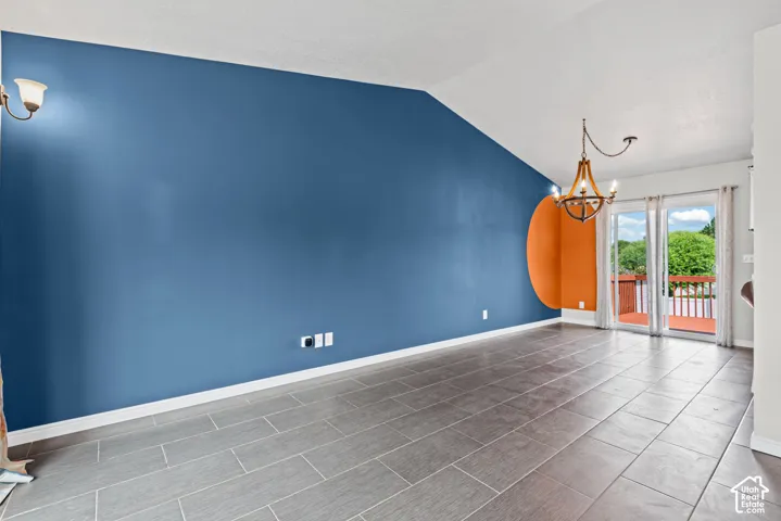 Vaulted ceiling, wall-mounted sconce, wood-finish chandelier, sliding glass doors, and tile flooring