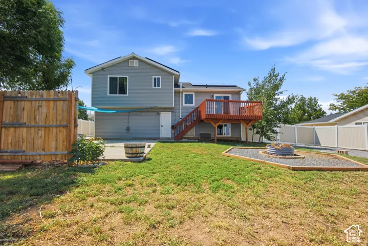 Expansive backyard featuring a wood privacy fence, concrete patio, a raised wood deck, and a fire pit area