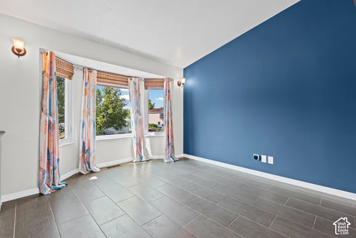 Bright corner bedroom featuring expansive windows with natural light, deep blue accent wall, and herringbone-pattern tile flooring