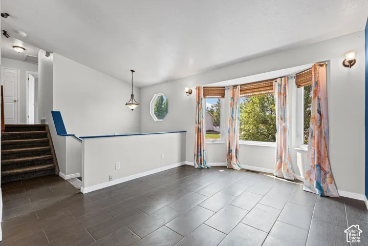 Expansive bay window, octagonal accent window, dark tile flooring, staircase with carpeted treads, and a polished nickel pendant light fixture
