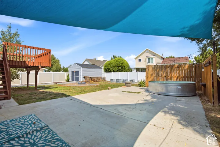 Paved patio with a galvanized metal soaking tub, wood privacy fencing, a raised deck with stairs, a storage shed, and a vinyl perimeter fence