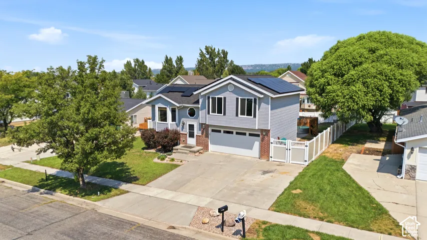 Two-story residence featuring light gray siding, a dark shingle roof with solar panels, an attached garage, and a white privacy fence