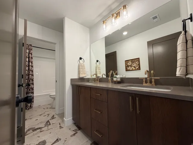 Spacious bathroom featuring a double vanity with stone-finish countertop, dual under-mount sinks, and bronze-finish fixtures