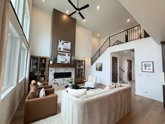 Great room featuring soaring ceilings, a modern fireplace with stone surround, wood-finish flooring, a contemporary ceiling fan, and an open staircase with a black metal railing