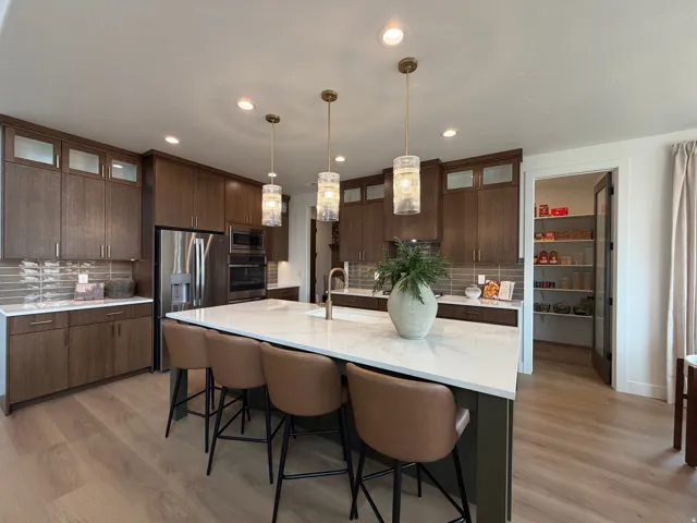 Modern kitchen featuring a large center island with seating, stainless steel appliances, wood-finish flooring, and a walk-in pantry