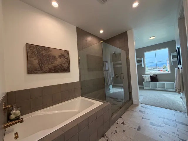 Luxurious primary bathroom showcasing a freestanding soaking tub with tile surround, frameless glass shower enclosure with dual showerheads, heated floor tile, recessed ceiling lighting, and a spa-like retreat with panoramic windows offering natural light