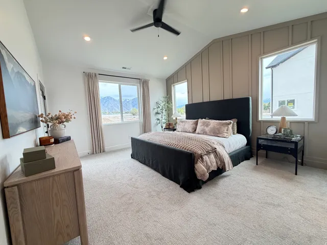 Vaulted ceilings featuring recessed lighting and a ceiling fan, a prominent accent wall with vertical paneling, and large windows with mountain scenery