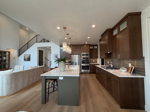 Open-concept kitchen and living area featuring light wood-finish flooring, a two-story ceiling, and a prominent staircase with black railings