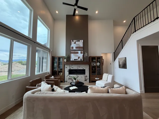 Spacious living area featuring a two-story ceiling, large windows, wood-finish flooring, a contemporary fireplace with a stone surround, and an open staircase with a metal railing