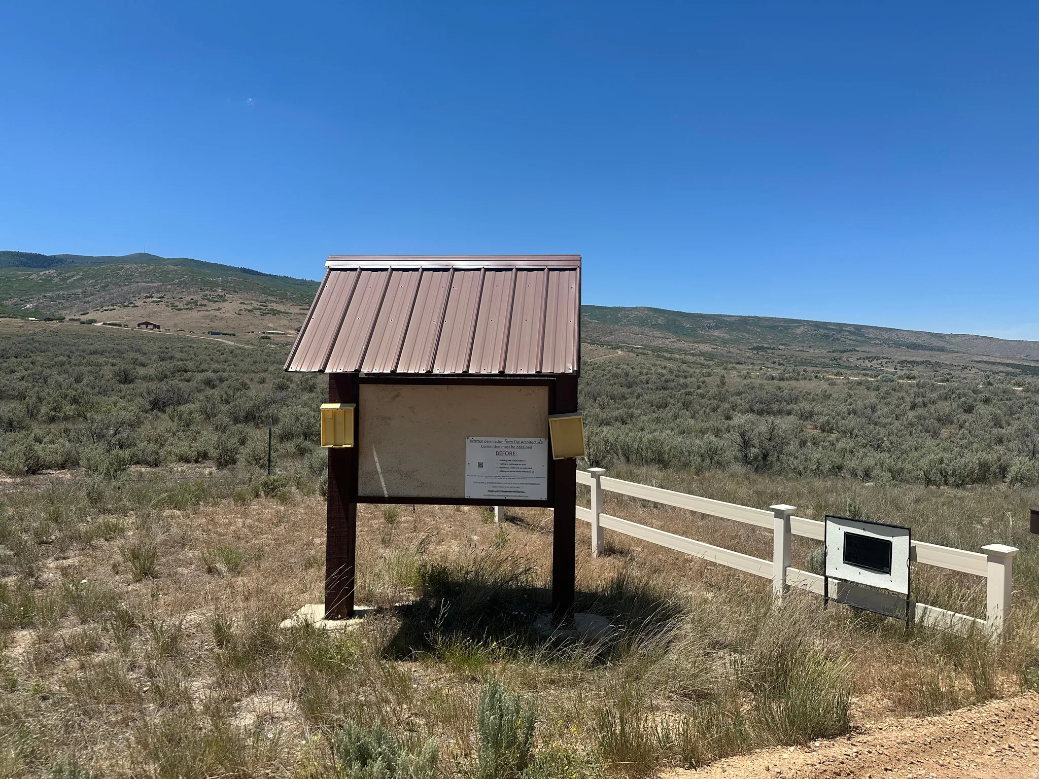 Informational kiosk with a brown metal roof, set against a backdrop of rolling hills and natural brush