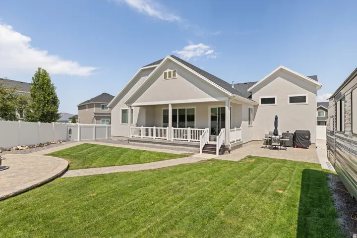 Expansive backyard featuring a manicured lawn, a large paver patio, a covered patio with white railing, and a vinyl privacy fence