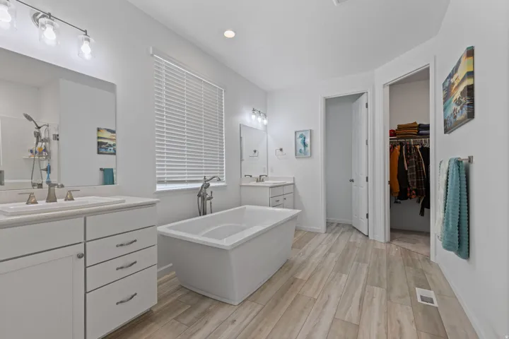 Contemporary bath featuring a freestanding soaking tub with floor-mounted faucet, dual vanities with white cabinetry and integrated sinks, and wood-finish tile flooring
