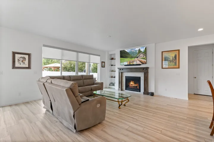 Spacious living area featuring wood-finish flooring, a fireplace with a wood mantle and stone surround, and built-in shelving
