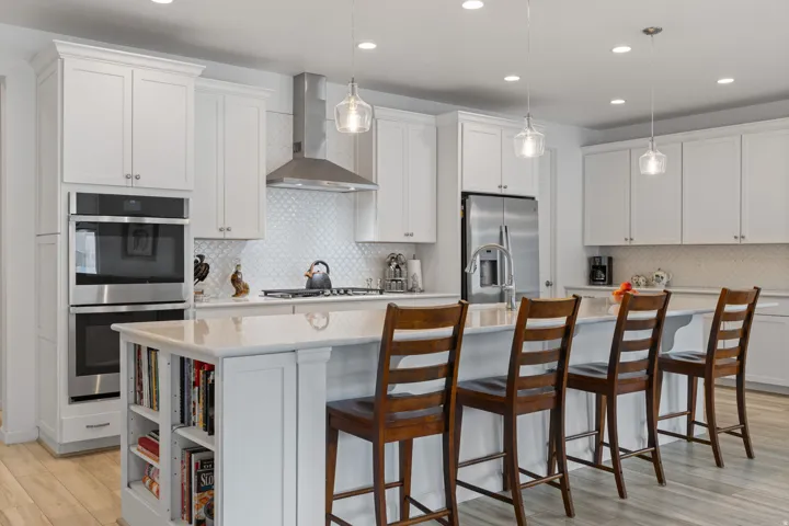 Kitchen featuring a large island with counter seating, stainless steel appliances, white shaker cabinetry, pendant lighting, and wood-finish flooring