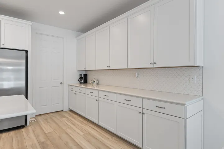 Extensive white cabinetry with silver hardware, light-toned countertops, and a decorative scallop-patterned backsplash