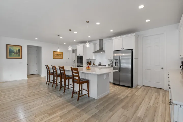 Spacious kitchen featuring an expansive center island with seating, white shaker cabinetry, stainless steel appliances, and wood-finish flooring