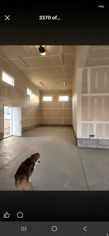Spacious garage featuring a concrete floor, multiple windows providing natural light, exposed drywall, and two entry doors