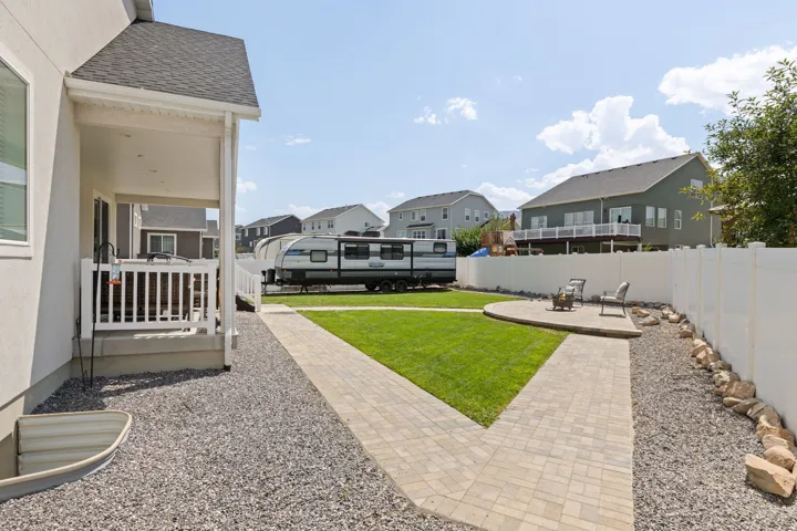 Expansive outdoor living area featuring a covered patio, paver walkway, manicured lawn, and a circular paver patio with a white privacy fence