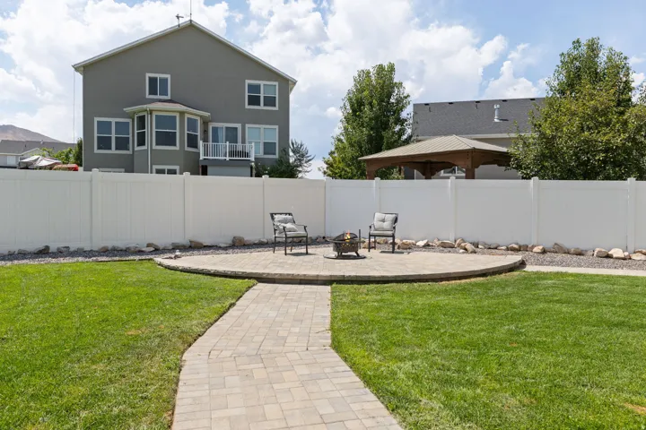 Expansive backyard featuring a paver patio with a circular fire pit area, a paver pathway, and a vinyl privacy fence