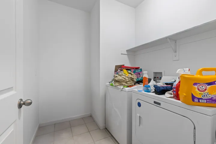 Dedicated laundry area featuring white appliances, a white wall-mounted shelf, and tiled flooring