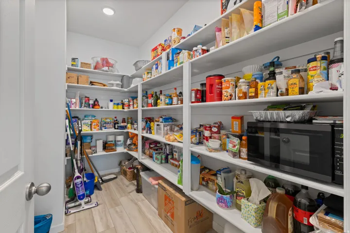 Spacious walk-in pantry featuring extensive built-in shelving, recessed ceiling lighting, and wood-finish flooring