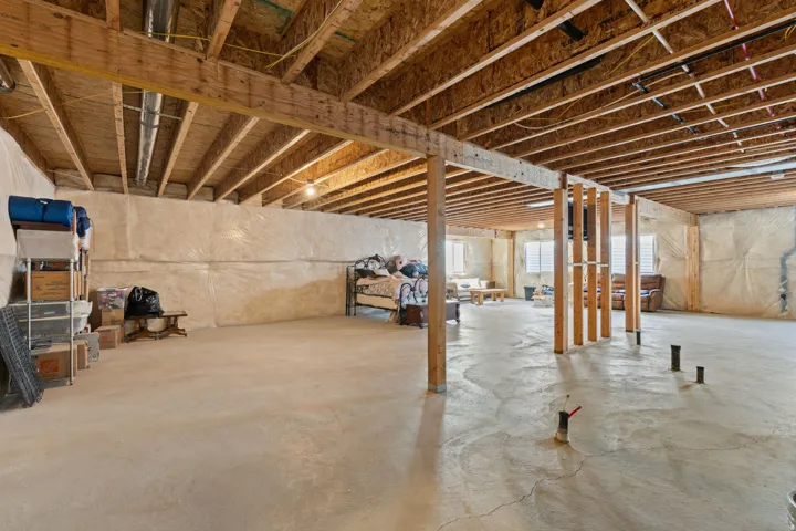 Spacious unfinished basement featuring exposed wood joists and support beams, concrete flooring, and perimeter insulation