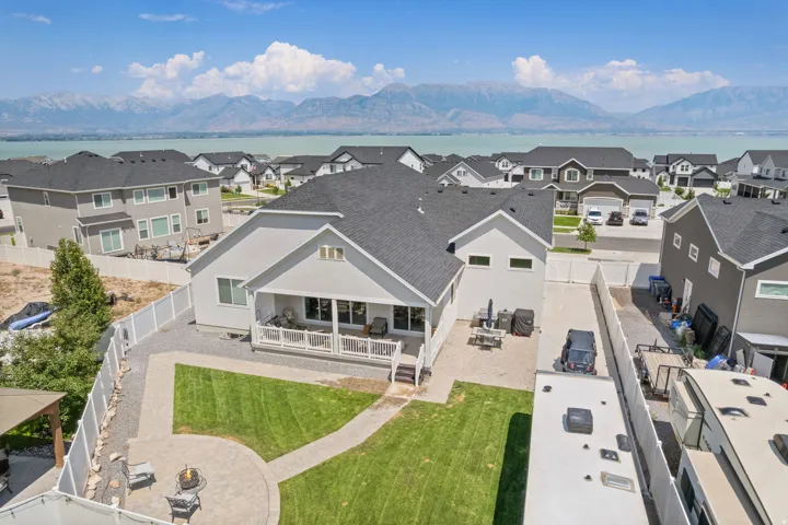 Backyard featuring a green lawn, paved patio areas, a fire pit, and a covered porch with white railings