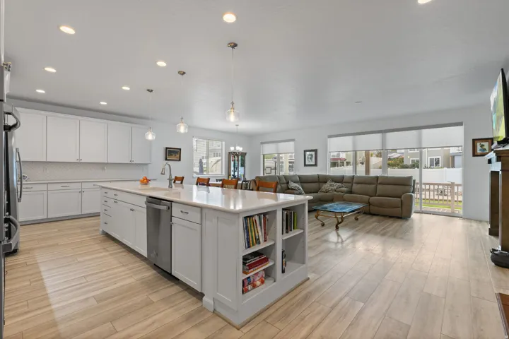 Open-concept living space featuring a spacious kitchen island with integrated shelving, light wood-finish flooring, white cabinetry, and stainless steel appliances