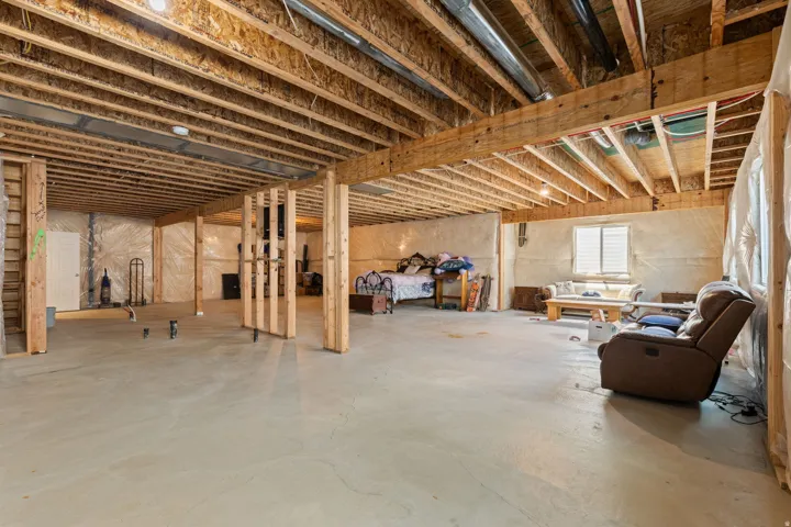 Unfinished basement with concrete flooring, exposed wood framing, and visible ceiling joists