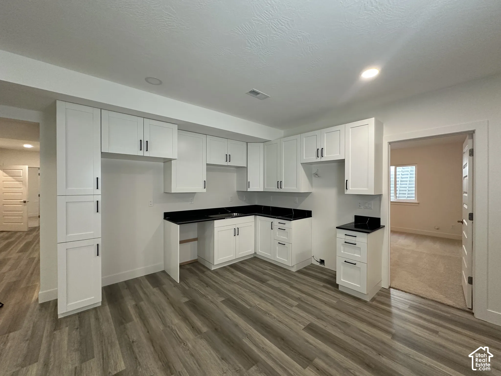 Kitchenette featuring white shaker cabinetry, dark countertops, wood-finish flooring, and recessed lighting