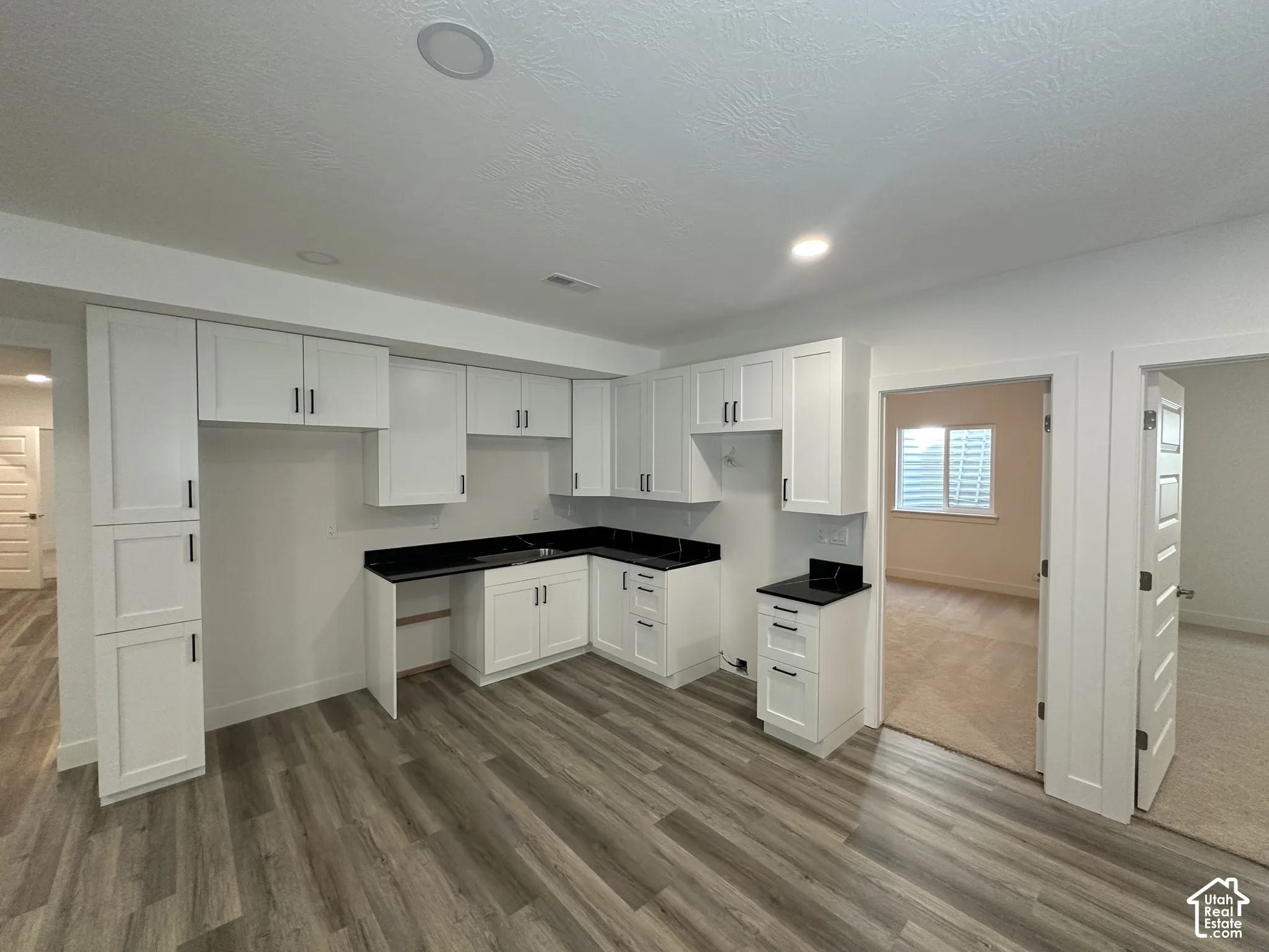 Spacious utility room featuring white cabinetry with black hardware, black laminate countertops, wood-finish flooring, and abundant storage throughout