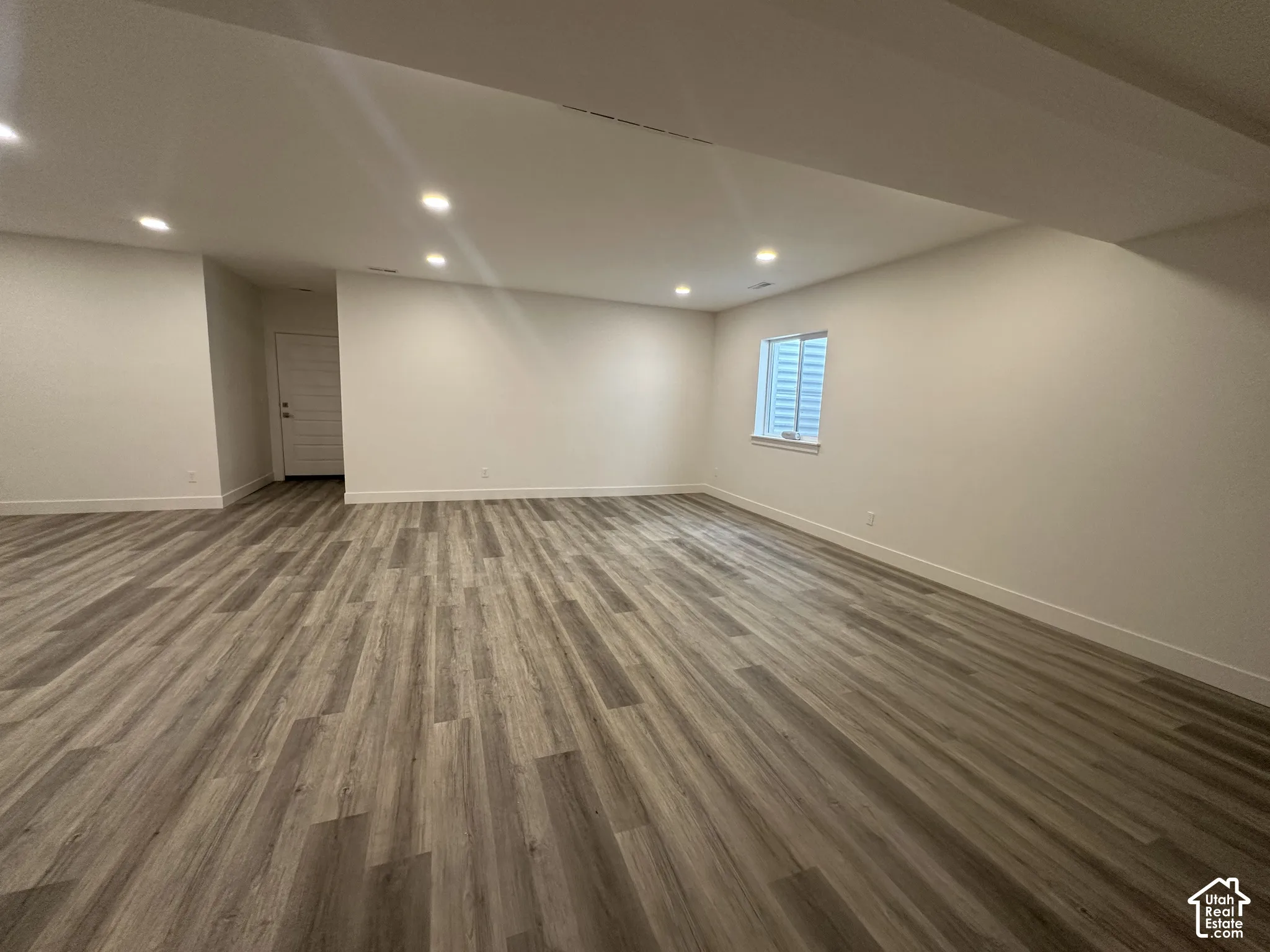 Expansive room featuring wood-finish flooring, recessed lighting, a window with horizontal blinds, and a white interior door