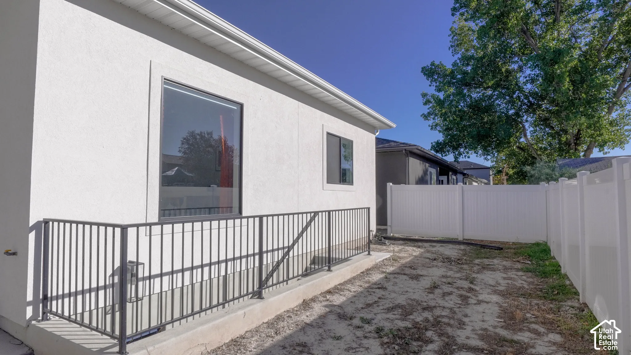 Newly constructed exterior wall with white stucco finish, featuring a large picture window, a smaller casement window, and a white vinyl privacy fence enclosing the property