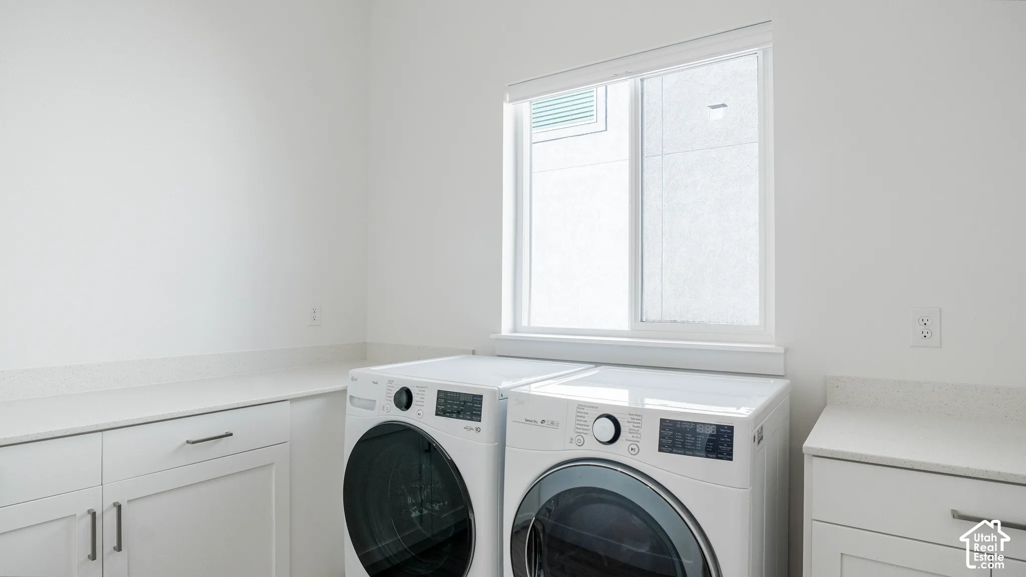 Laundry area featuring white cabinetry, light-toned countertops, and a window