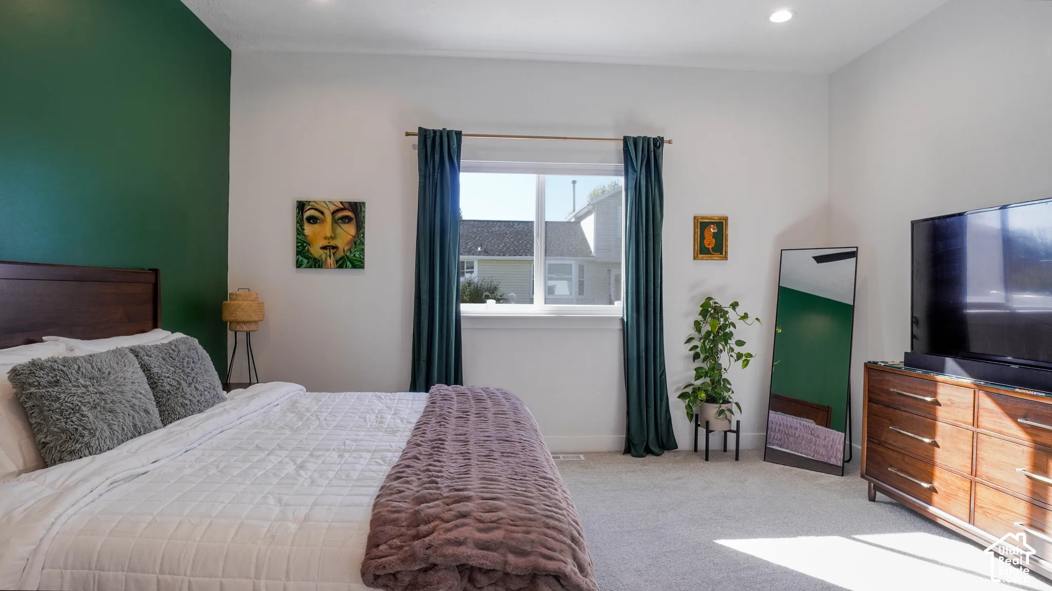 Spacious room featuring a dark wood headboard, a broad window with drapes, light-toned carpeting, a recessed ceiling light, and a wooden dresser