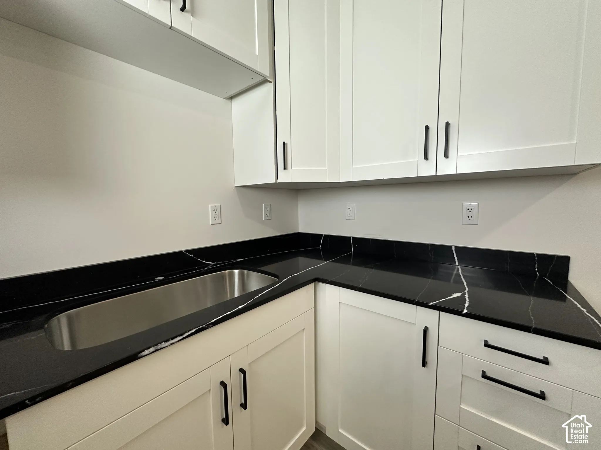 Modern kitchen or utility space featuring white shaker-style cabinetry with matte black hardware, black countertops with white veining, and an undermount stainless steel sink