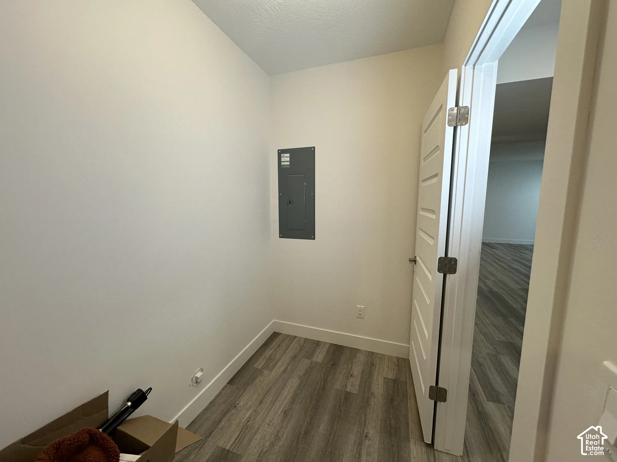 Compact utility space featuring light-toned walls, wood-finish flooring, a white five-panel door, and a visible electrical panel