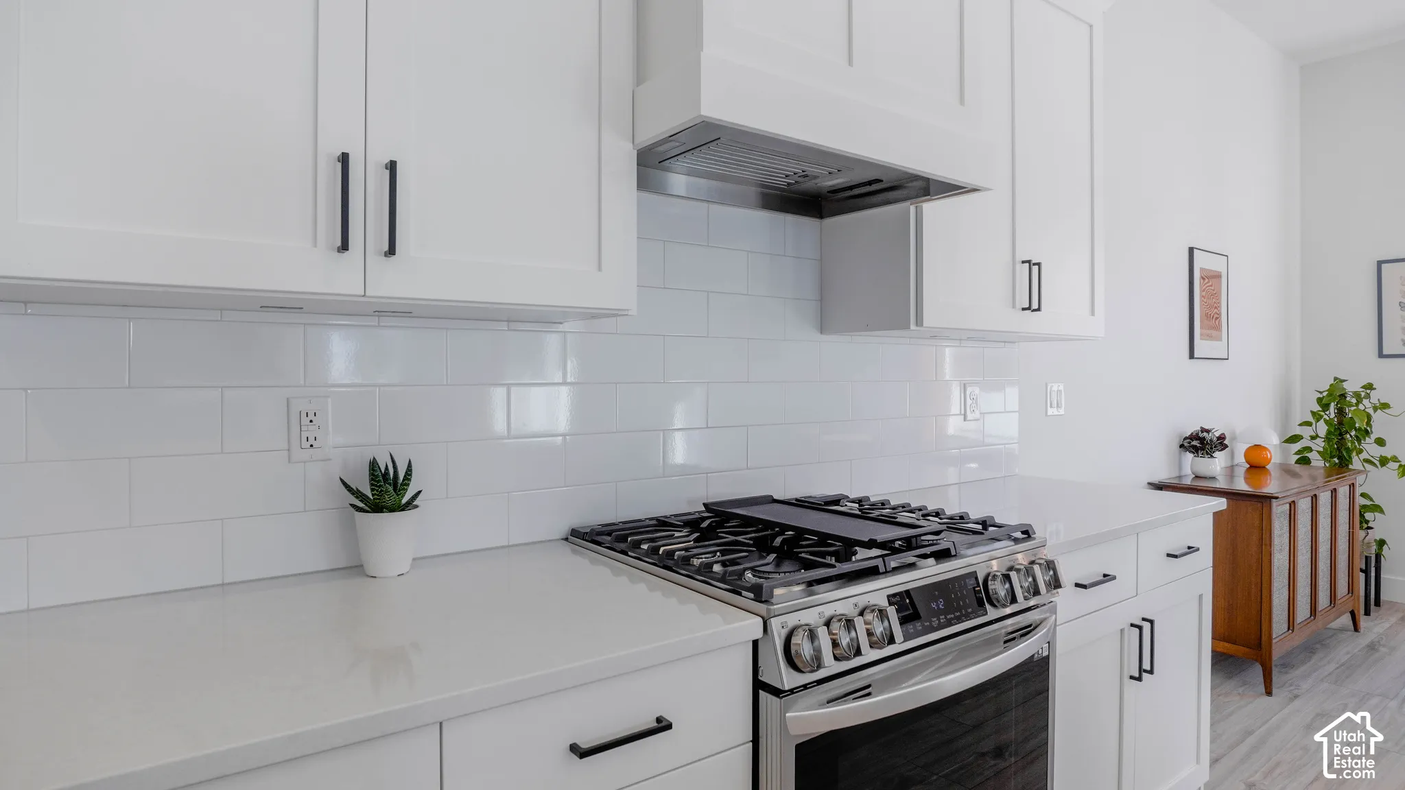 Modern kitchen featuring white shaker cabinetry, stainless steel range with a griddle, coordinating range hood, white subway tile backsplash, and light-toned countertops