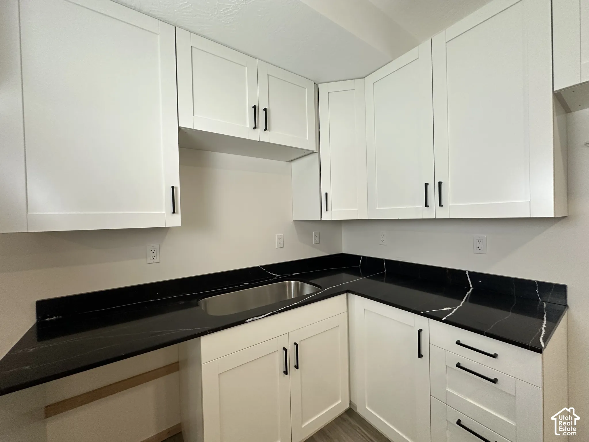 Contemporary kitchen featuring white shaker cabinetry with black hardware, dark countertops with white veining, and an undermount stainless steel sink