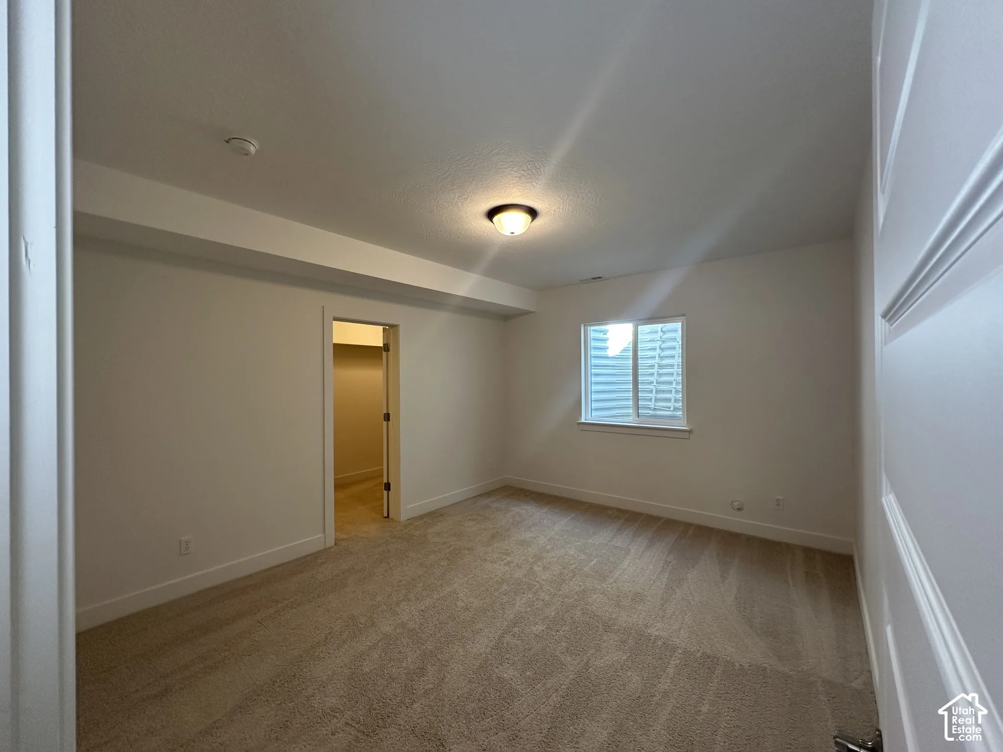 Spacious room featuring neutral carpeting, a ceiling-mounted light fixture, and a window with blinds