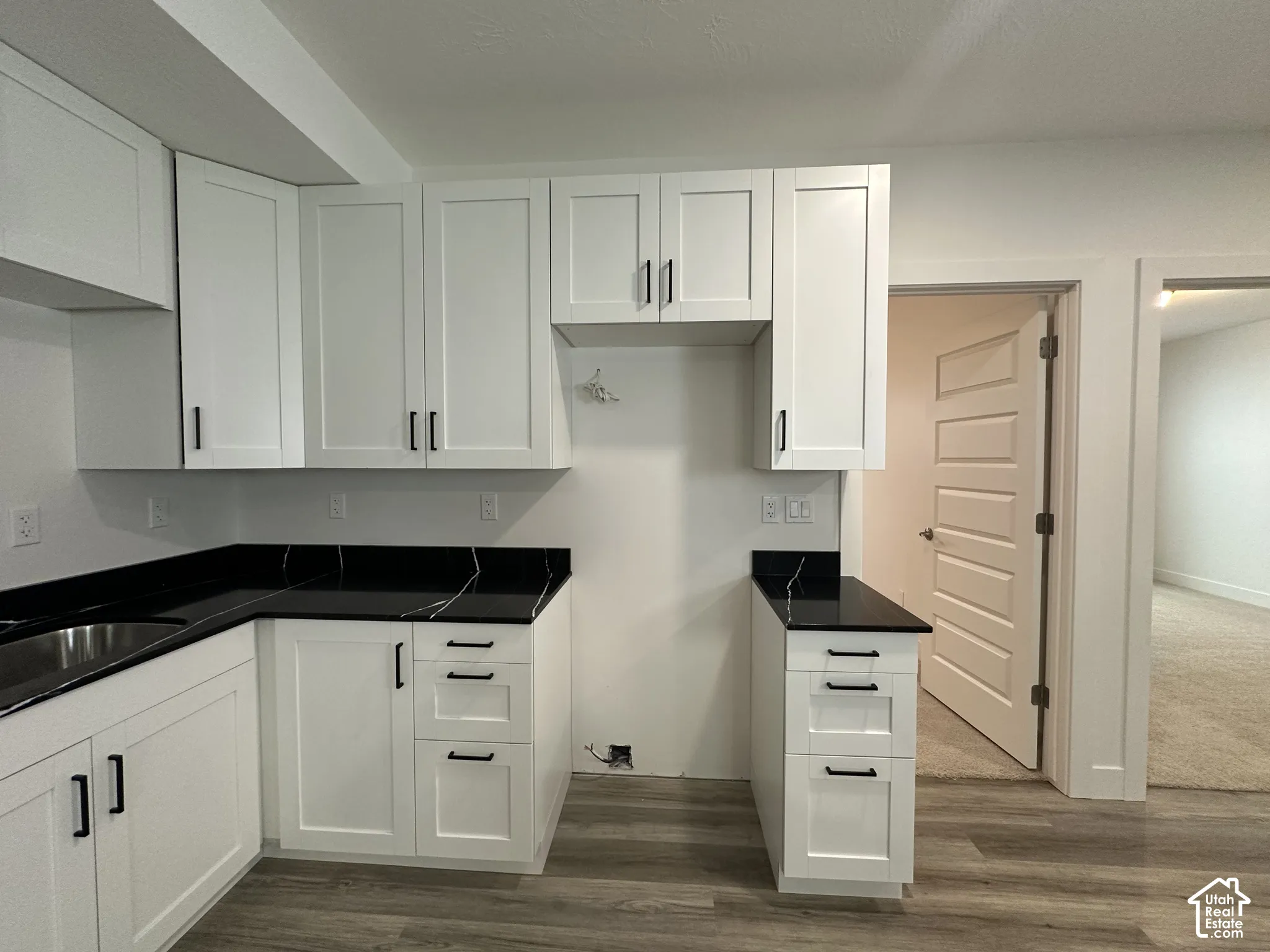 Modern kitchen featuring white shaker cabinetry, dark countertops with subtle veining, a stainless steel sink, and wood-finish flooring