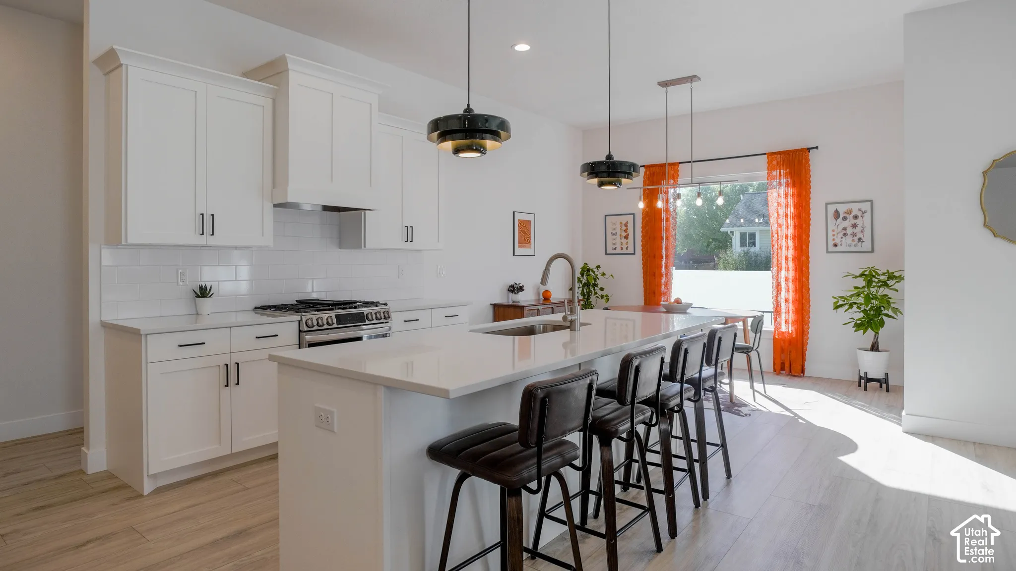 Contemporary kitchen featuring light wood-finish flooring, white cabinetry with black hardware, a gas range with a stainless steel vent hood, a white subway tile backsplash, and a large central island with an undermount sink