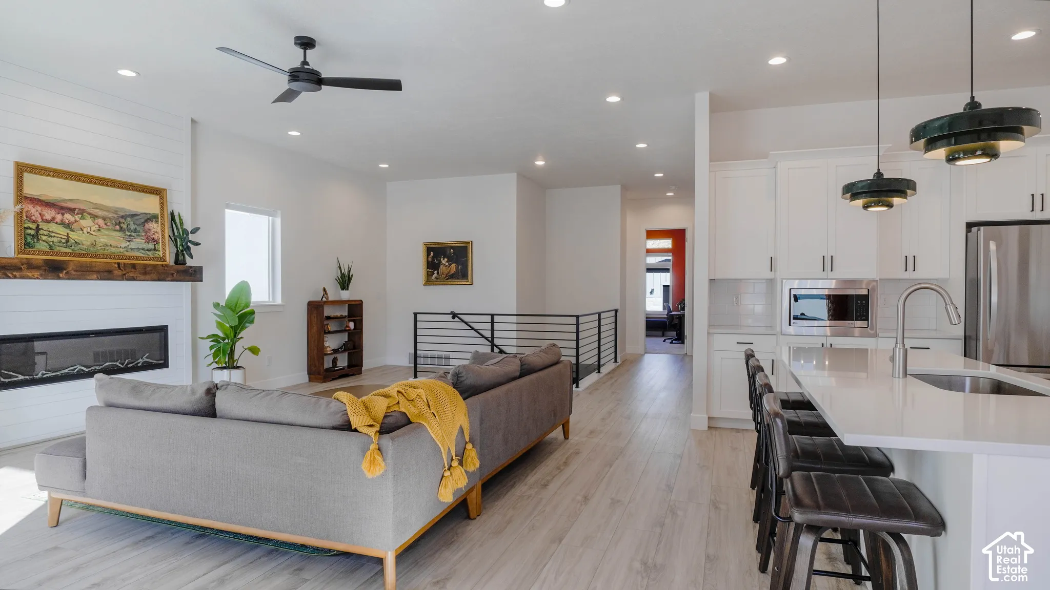 Open-concept living space featuring wood-finish flooring, a contemporary linear fireplace with a wood mantel, and an adjacent kitchen with white cabinetry